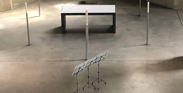 Drei Notenständer vor einer brennenden Kerze. Im Hintergrund eine Art Tisch